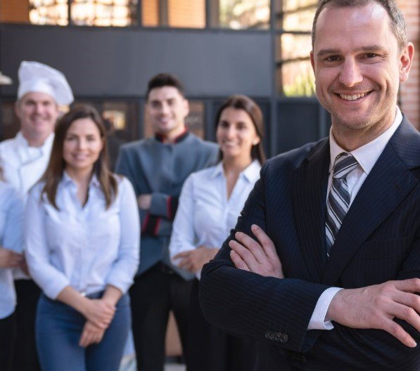 Management, chef and hotel staff standing outside hotel lobby